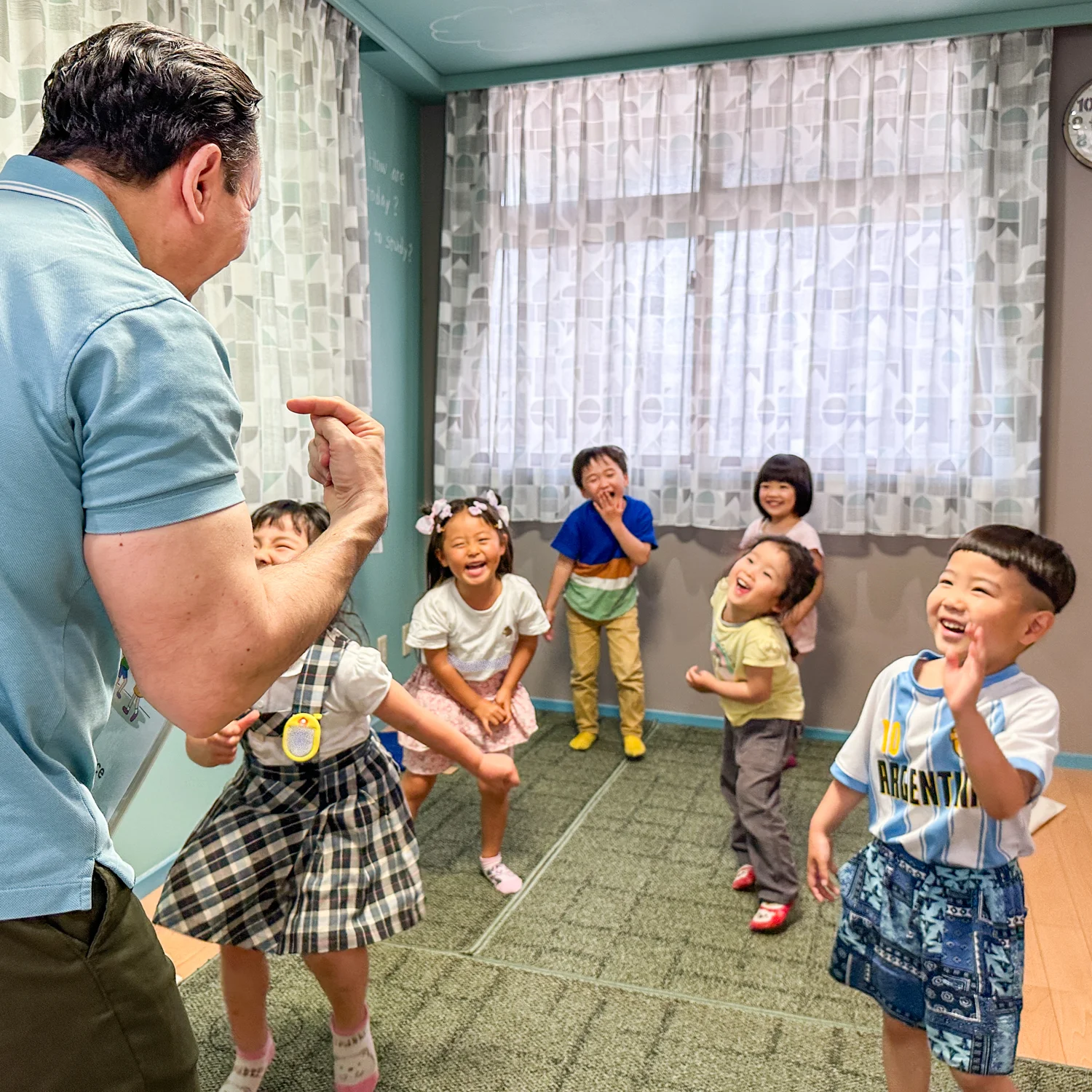 笑顔あふれる幼稚園児たちがケビン先生と一緒に英語を使って遊んでいる様子