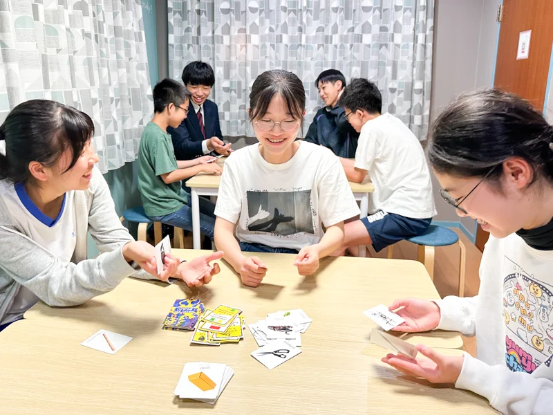 高松英会話ケビンズイングリッシュハウスで中学生たちが英会話グループレッスン中にゲームカードを使って楽しく英語を学んでいる写真